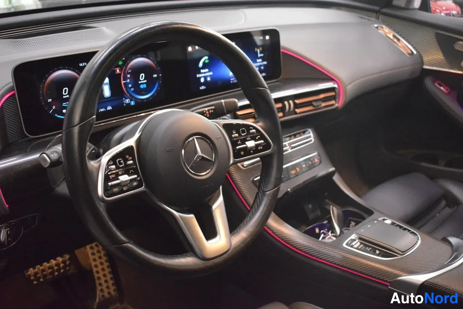 Muu: Ohjauspyörä ja Mercedes-Benzin merkkilogo, taustalla näyttö ja punainen tunnelmavalaistus.
