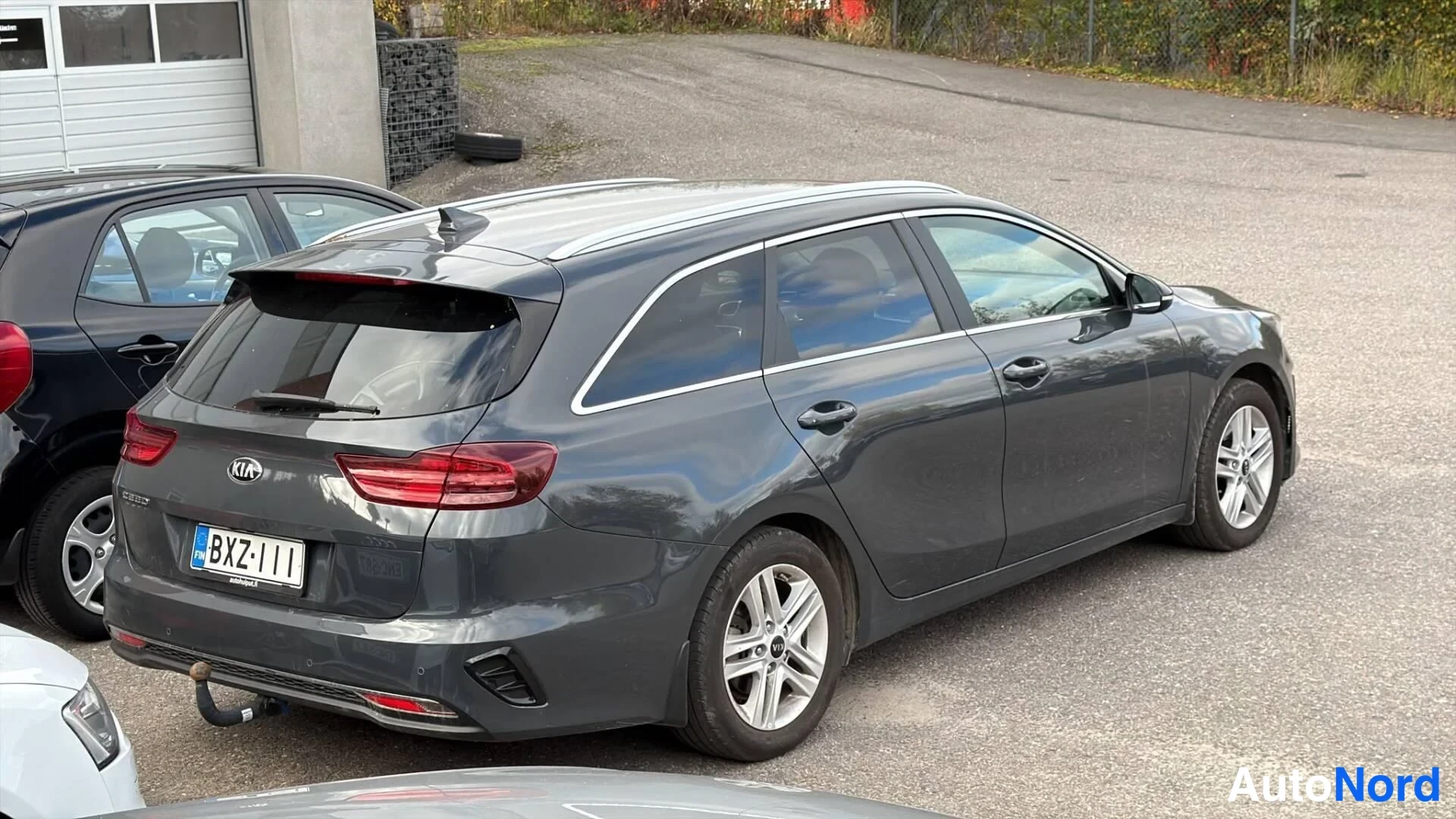 Takaviisto: Kia Ceed SW farmariauto tummanharmaana takaviistosta; rekisterikilpi, KIA-merkki takaluukussa, kattokaiteet, hopeavanteet ja vetokoulu näkyvät.