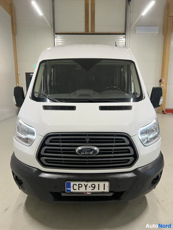 Edestä: Valkoisen Ford Transitin suora etunäkymä mustalla Ford-merkkiin päättyvällä säleiköllä ja rekisterikilvellä.