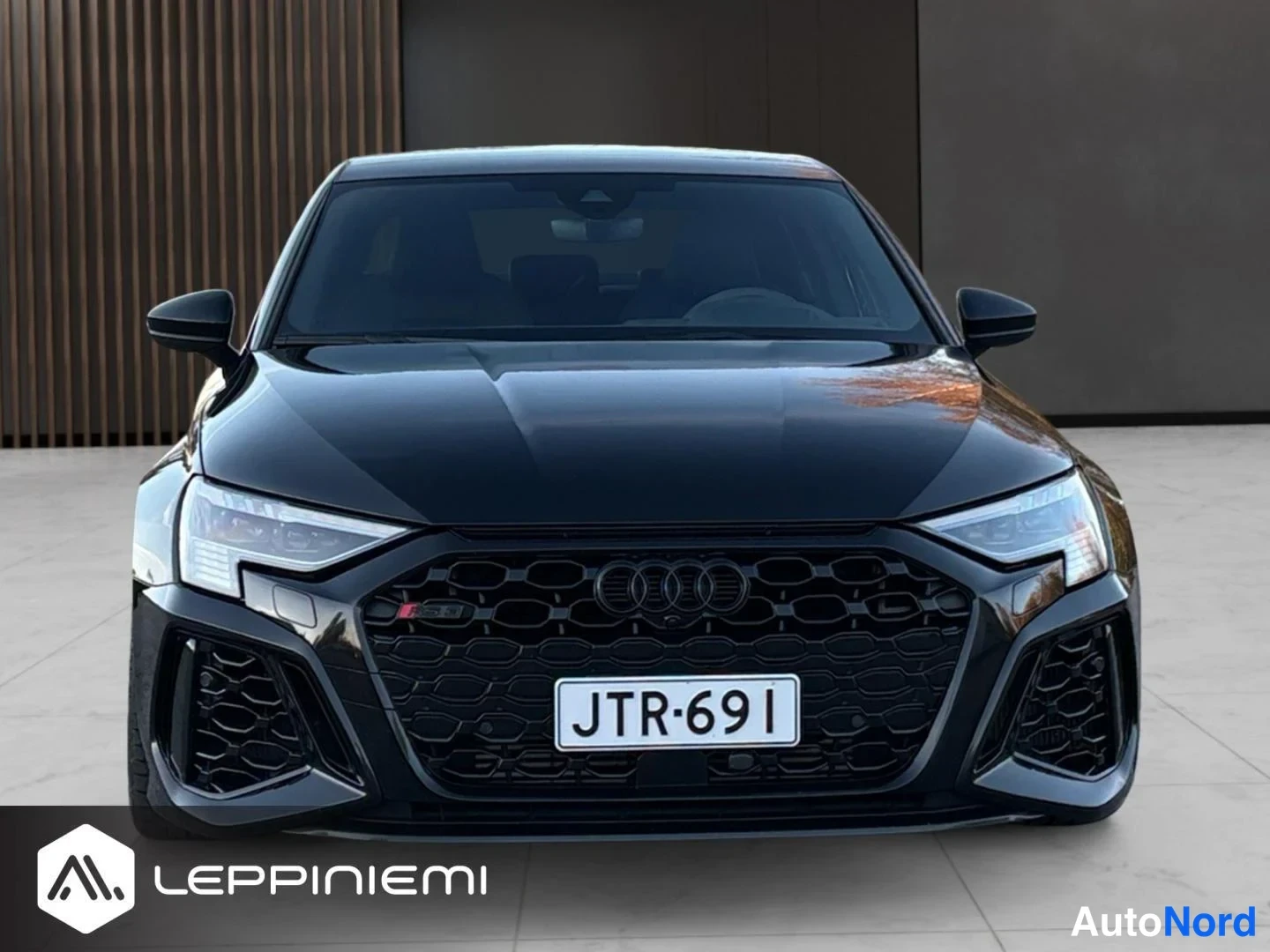 Edestä: Musta Audi A3 suoraan edestä, iso verkkokori ja rekisteri.
