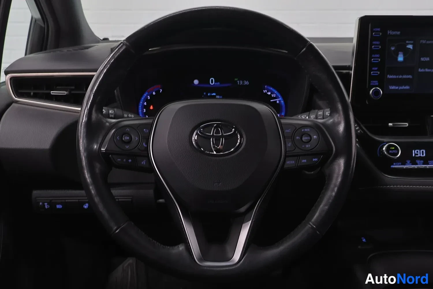 Yksityiskohta: Rattin ja kojelaudan näkymä: Toyota-merkillinen monitoimiratti, digitaalinen mittaristo ja kosketusnäytöllinen infotainment-järjestelmä.