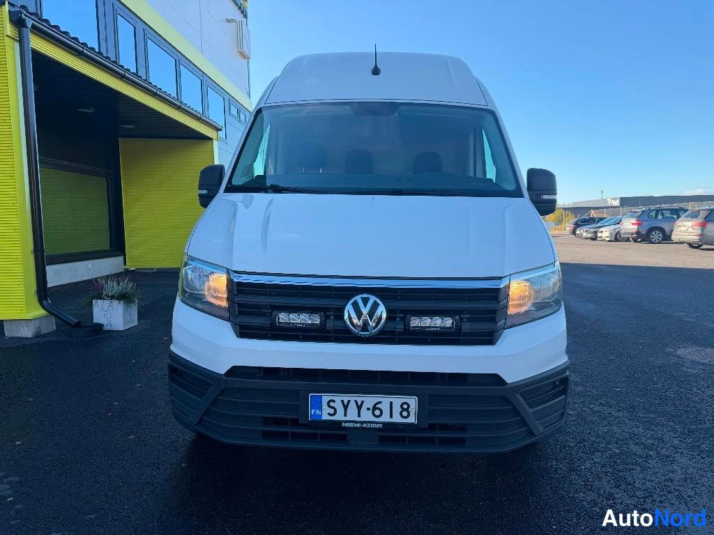 Edestä: Valkoisen Volkswagen Crafter -pakettiauton etunäkymä, etugrilli ja valoja näkyvät, rekisteritunnus.