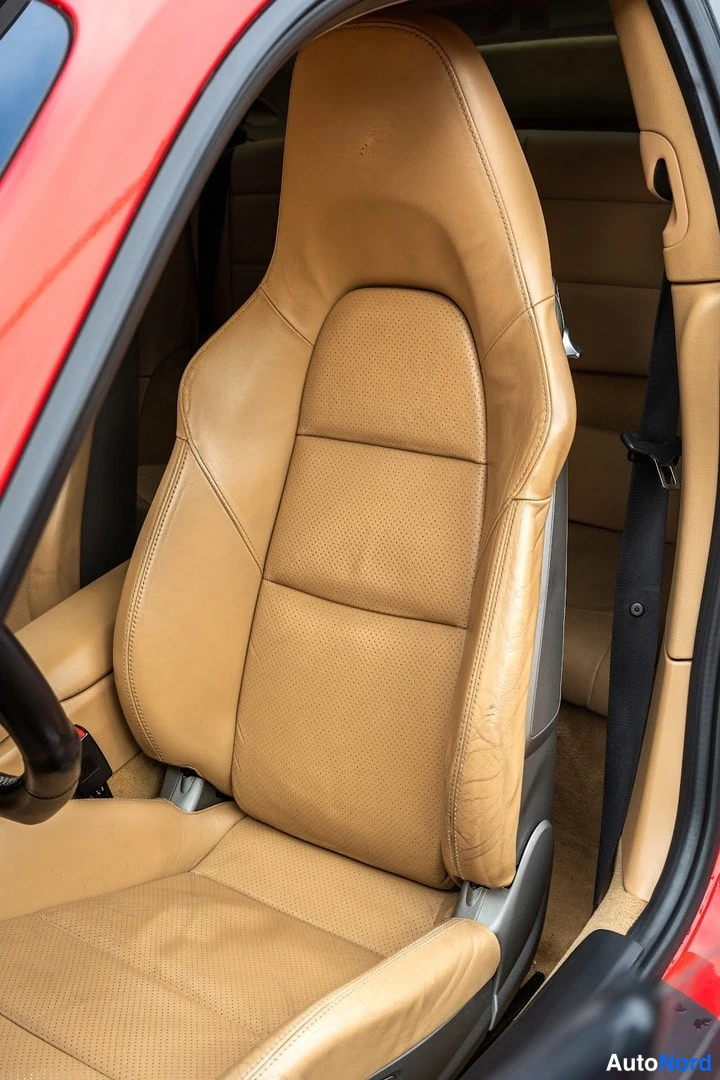 Yksityiskohta: Punaisen auton kaksipaikkainen beige urheiluistuin autonoven kautta kuvattuna, istuin pehmeää nahkaa.