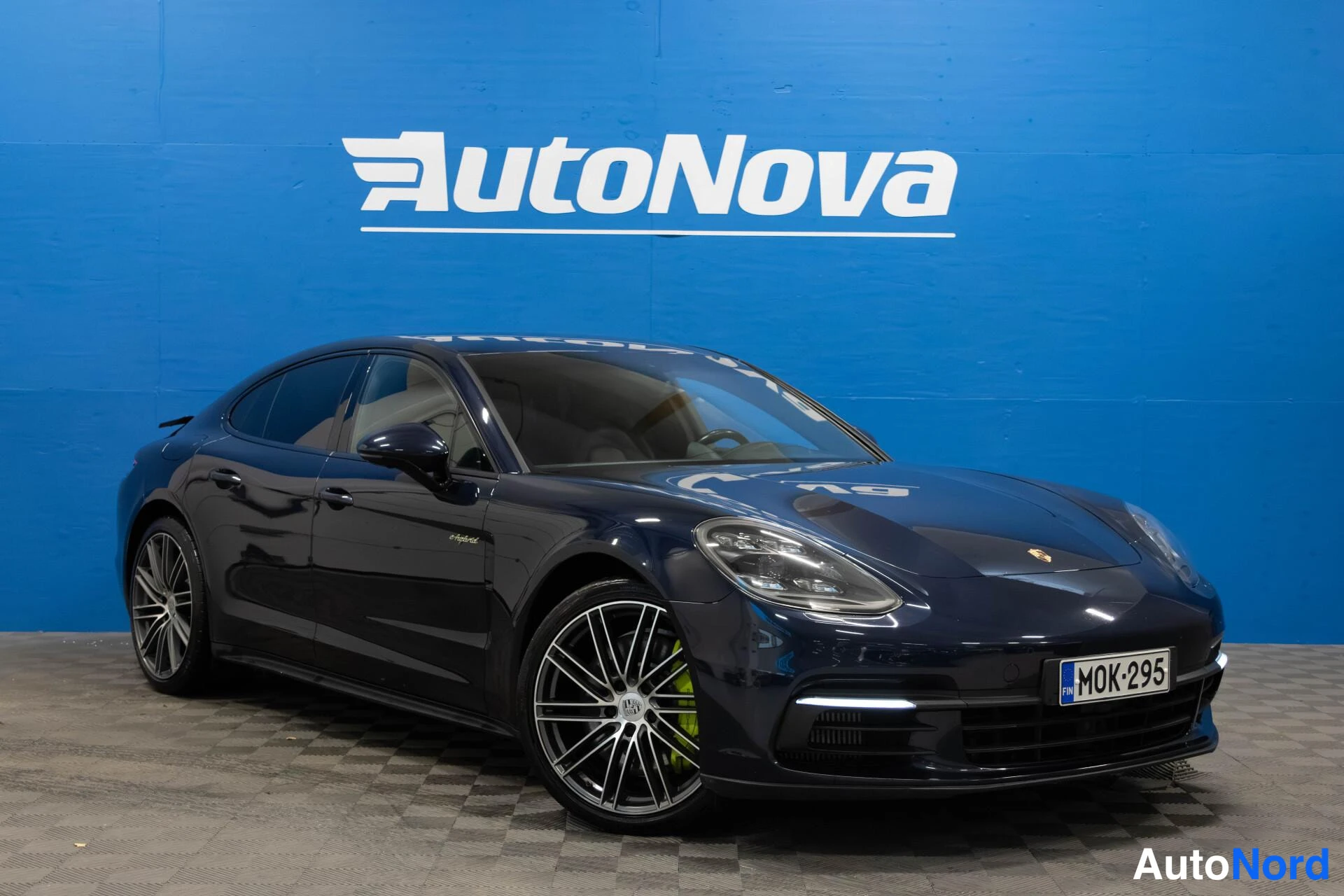 Etuviisto, nokka oikealle: Tummansininen Porsche Panamera etukulmasta oikealta, rekisteritunnus, sininen tausta.
