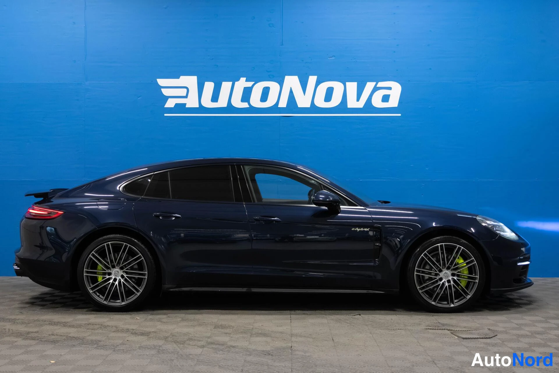 Etuviisto, nokka oikealle: Tummansininen Porsche Panamera sivulta, rekisteritunnus, keltainen jarrusatula näkyy etupyörässä.
