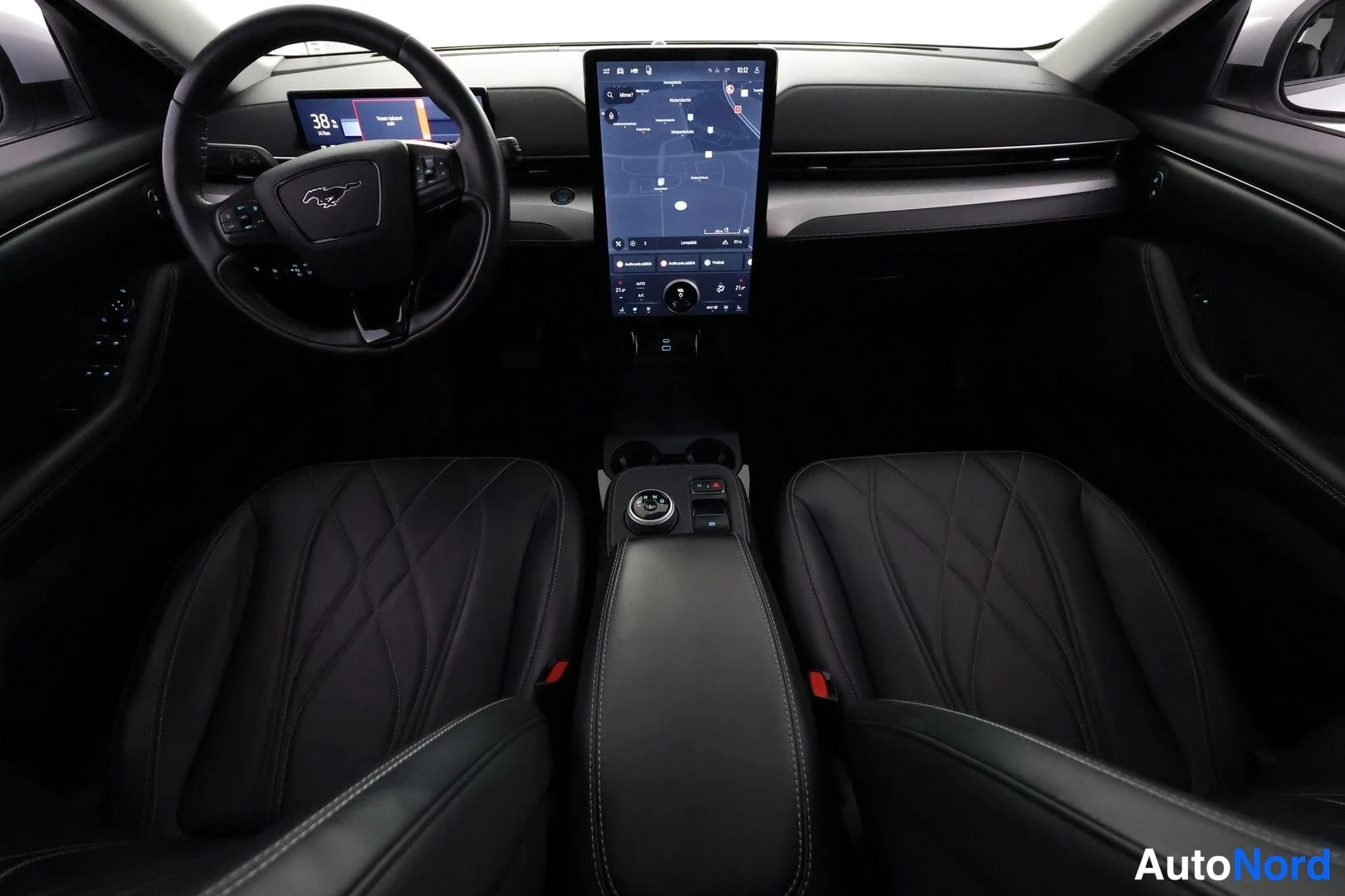 Yksityiskohta: Mustang Mach-E:n kojelauta ja ohjaamo suoraan edestä: ratissa Mustang-logo, kartta näyttävä suuri keskinäytön ja mustat nahkaiset etuistuimet.
