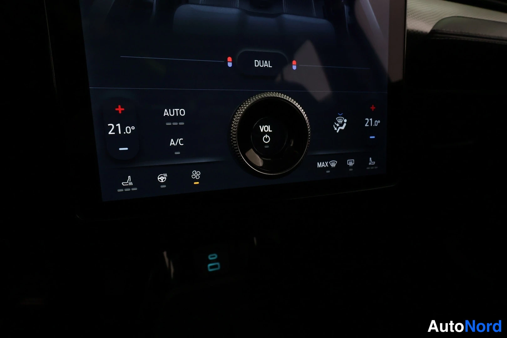 Yksityiskohta: Tarkka kuva auton näytön ilmastointiasetuksista: vasemmalla + ja - merkinnät 21.0 asteeseen, keskellä DUAL-teksti ja säätöpyörä, oikeassa 21.0 astetta. AUTO- ja