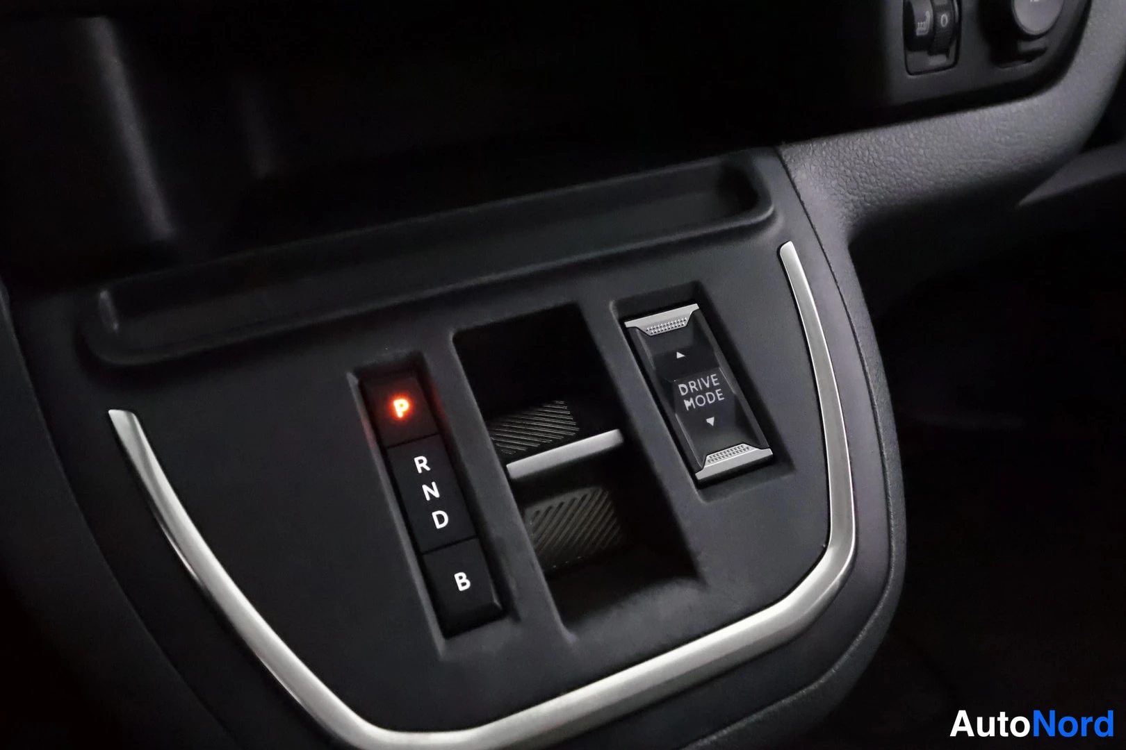 Muu: Automaattivaihteen P R N D B painikepaneeli, jossa P-merkki valaistu punaisella, ja viereinen DRIVE MODE -kytkin.
