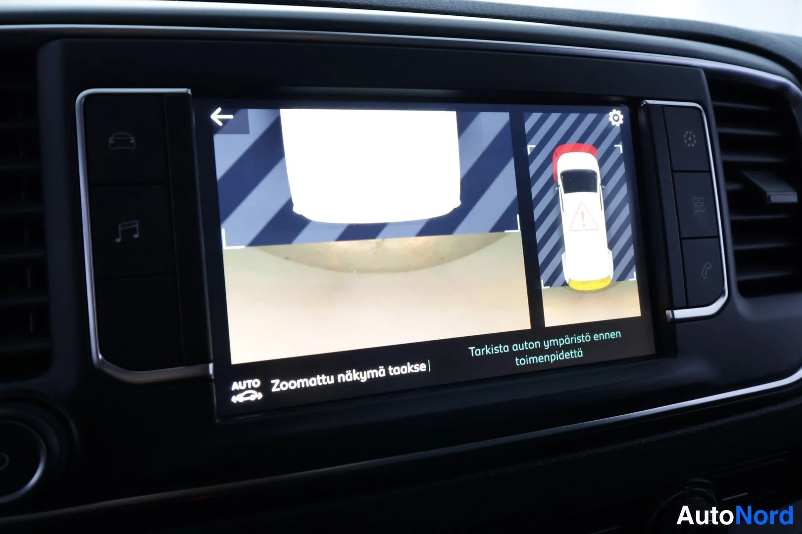 Muu: Kojelaudan infotainment-näyttö, jolla näkyy takaperinpyörähdyskamera ja teksti 'Zoomattu näkymä taakse'.
