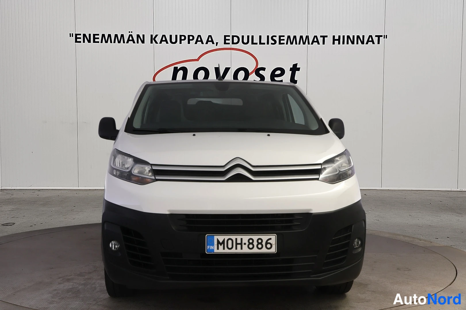 Edestä: Suora etänäkymä valkoisesta pakettiautosta: etusäleikkö, etavalot ja rekisteritunnus näkyvät.