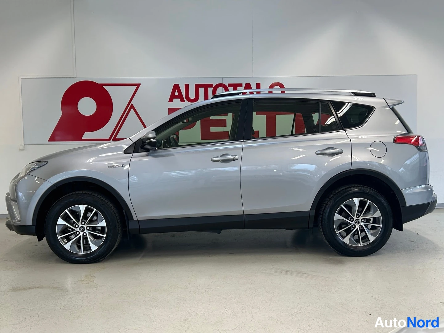 Sivulta: Sivukulmanäkymä hopeanvärisen Toyota RAV4:n vasemmasta sivusta sisätiloissa, neljä ovea ja kattotelineet näkyvissä.
