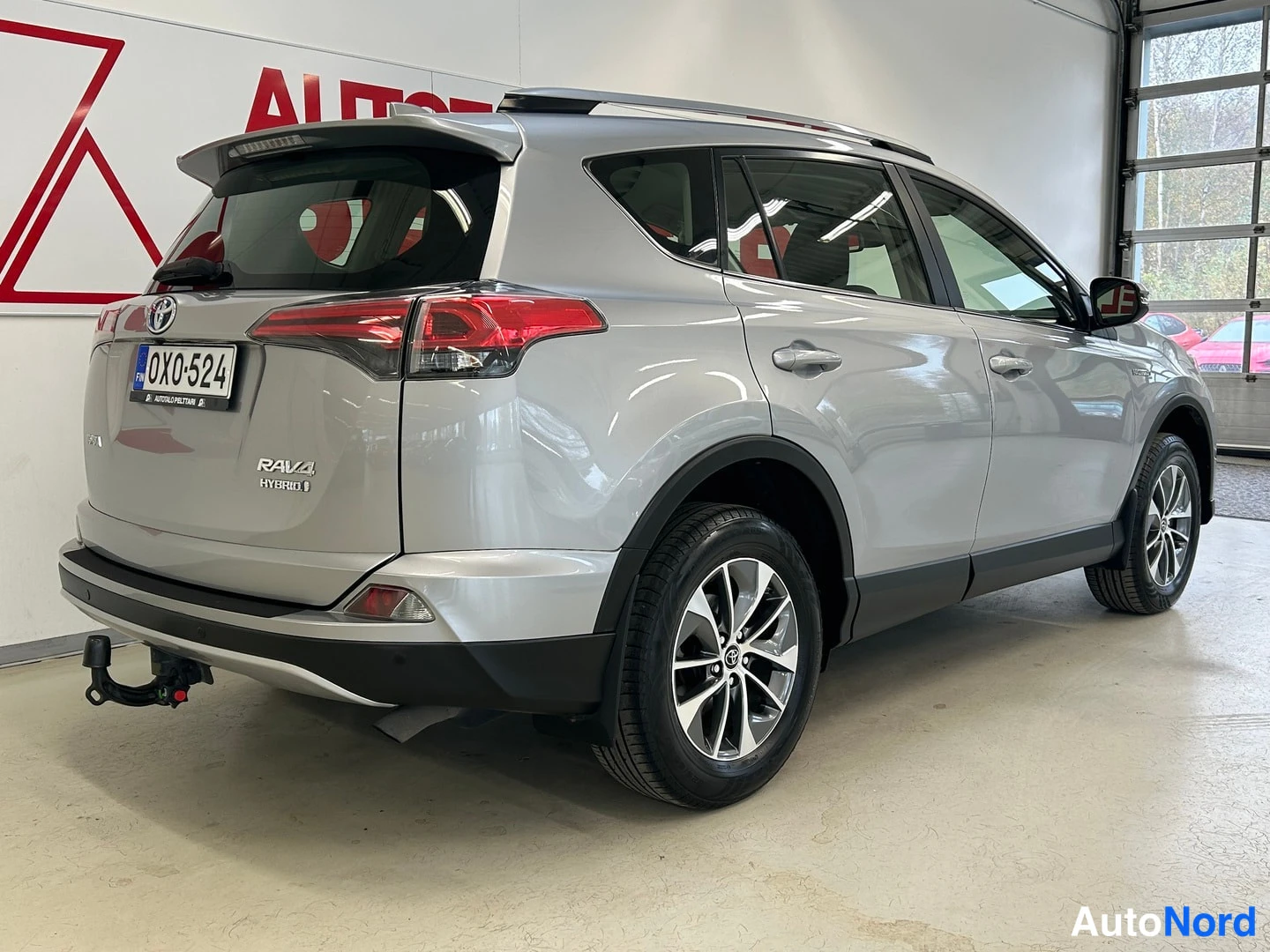 Takaviisto: Hopeanvärinen Toyota RAV4 takaa oikealta yläviistosta kuvattuna; rekisterikilpi OX0-524, RAV4 HYBRID-teksti ja taakse kääntyvä lukki näkyvät.