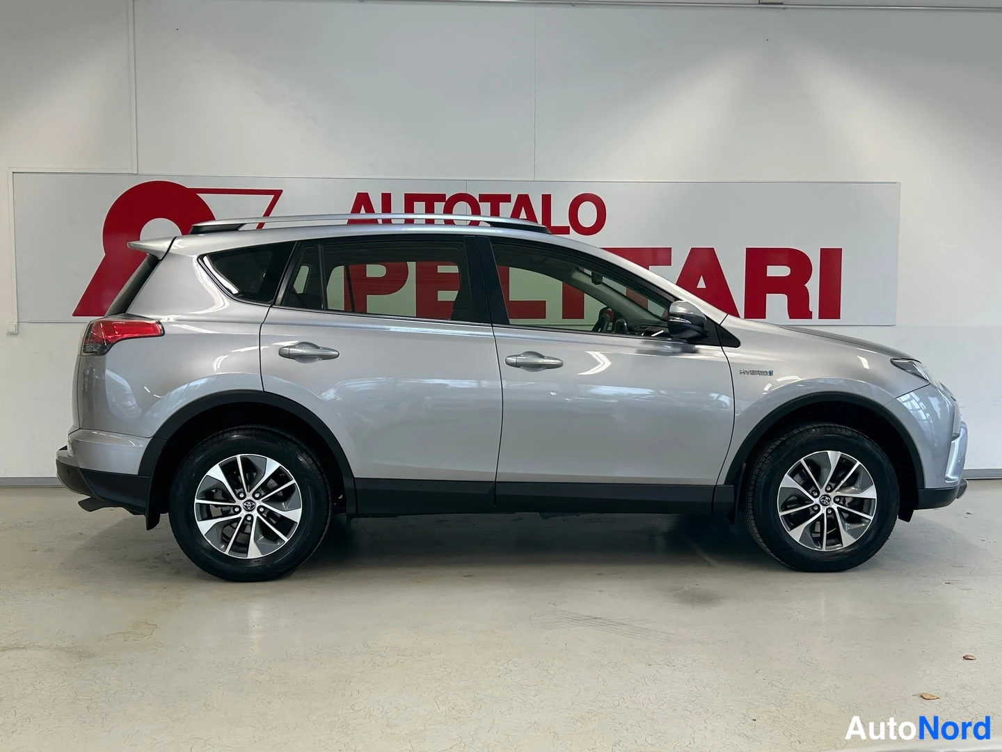 Sivulta: Hopeanvärinen Toyota RAV4 sivulta kuvattuna sisätiloissa; AUTOTALO PELTTARI -kyltti taustalla.