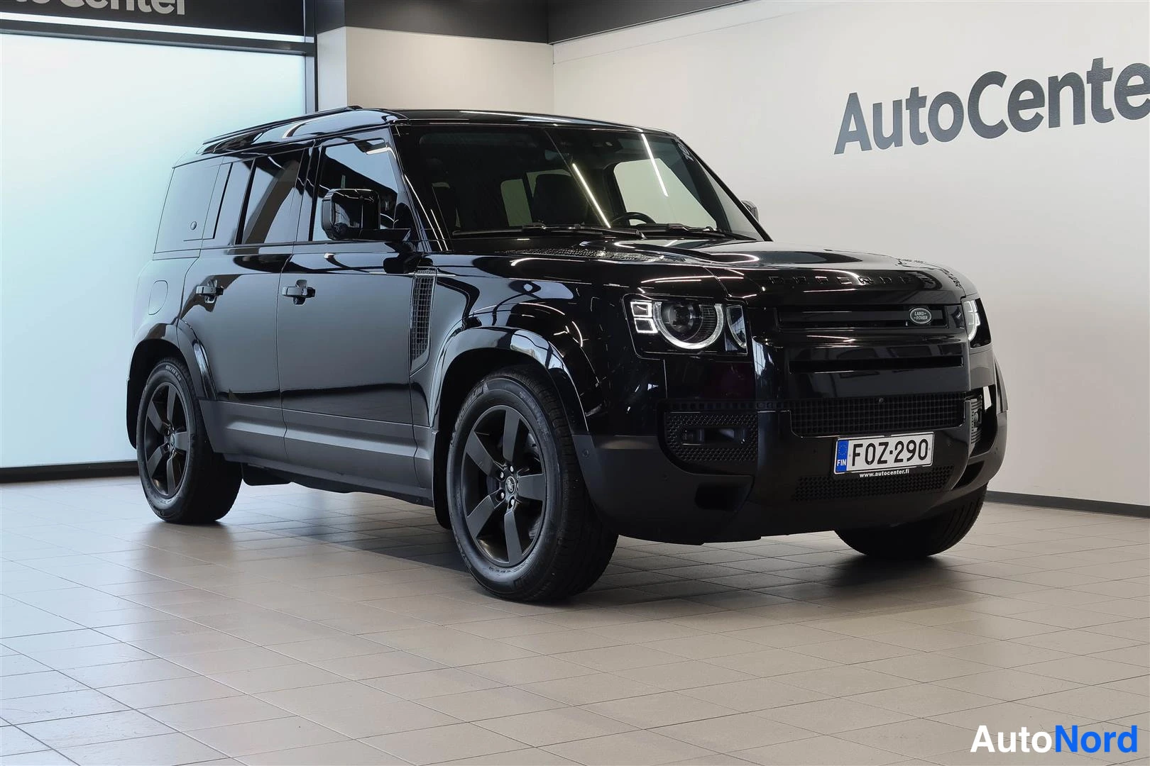 Etuviisto, nokka vasemmalle: Musta Land Rover Defender autohallissa, etukulmanäky vaaka-alueelta.