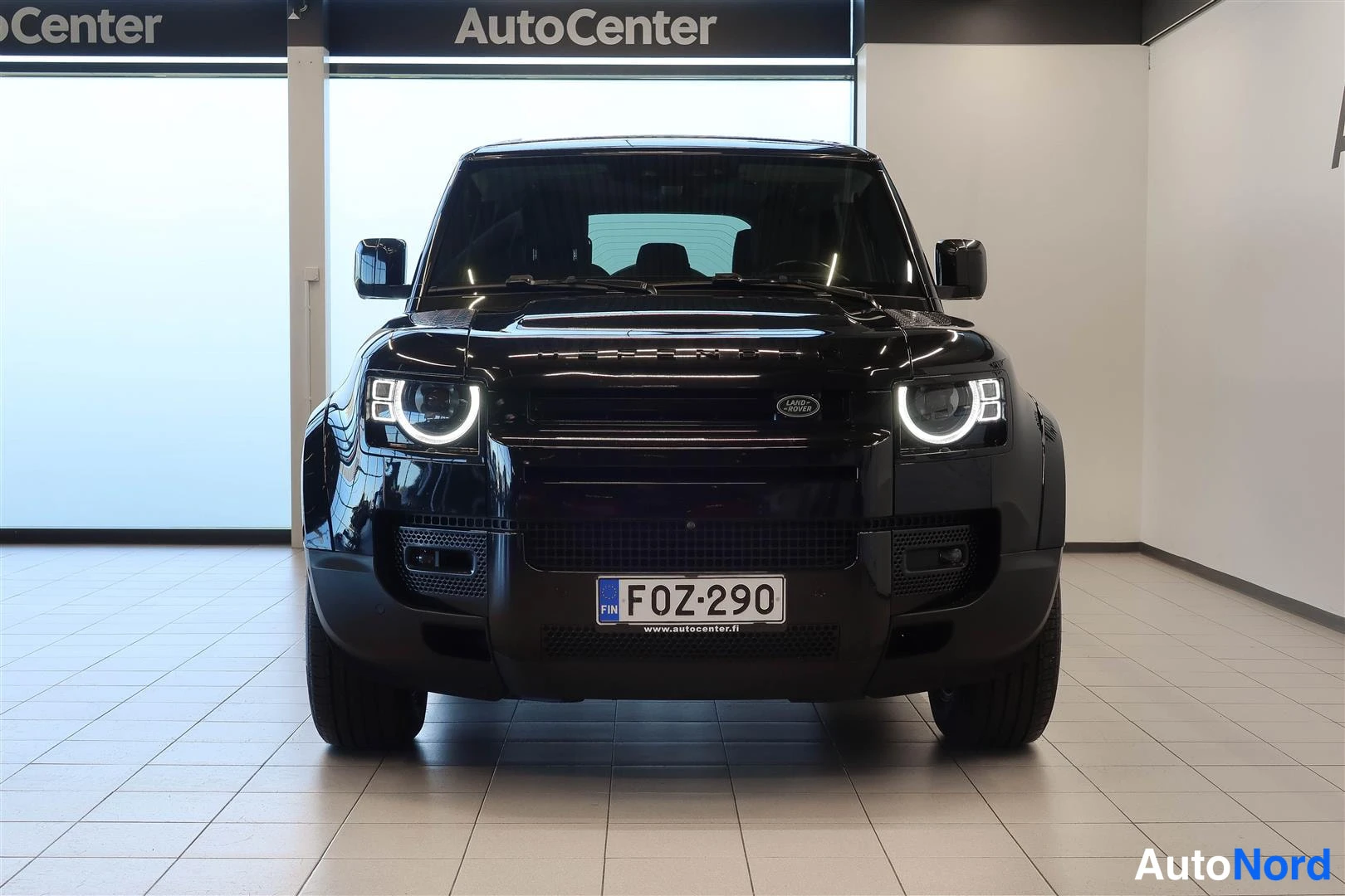 Edestä: Musta Land Rover Defender suoraan edestäpäin, kierretyt etuvalot palavat, rekisterikilpi F0Z-290.