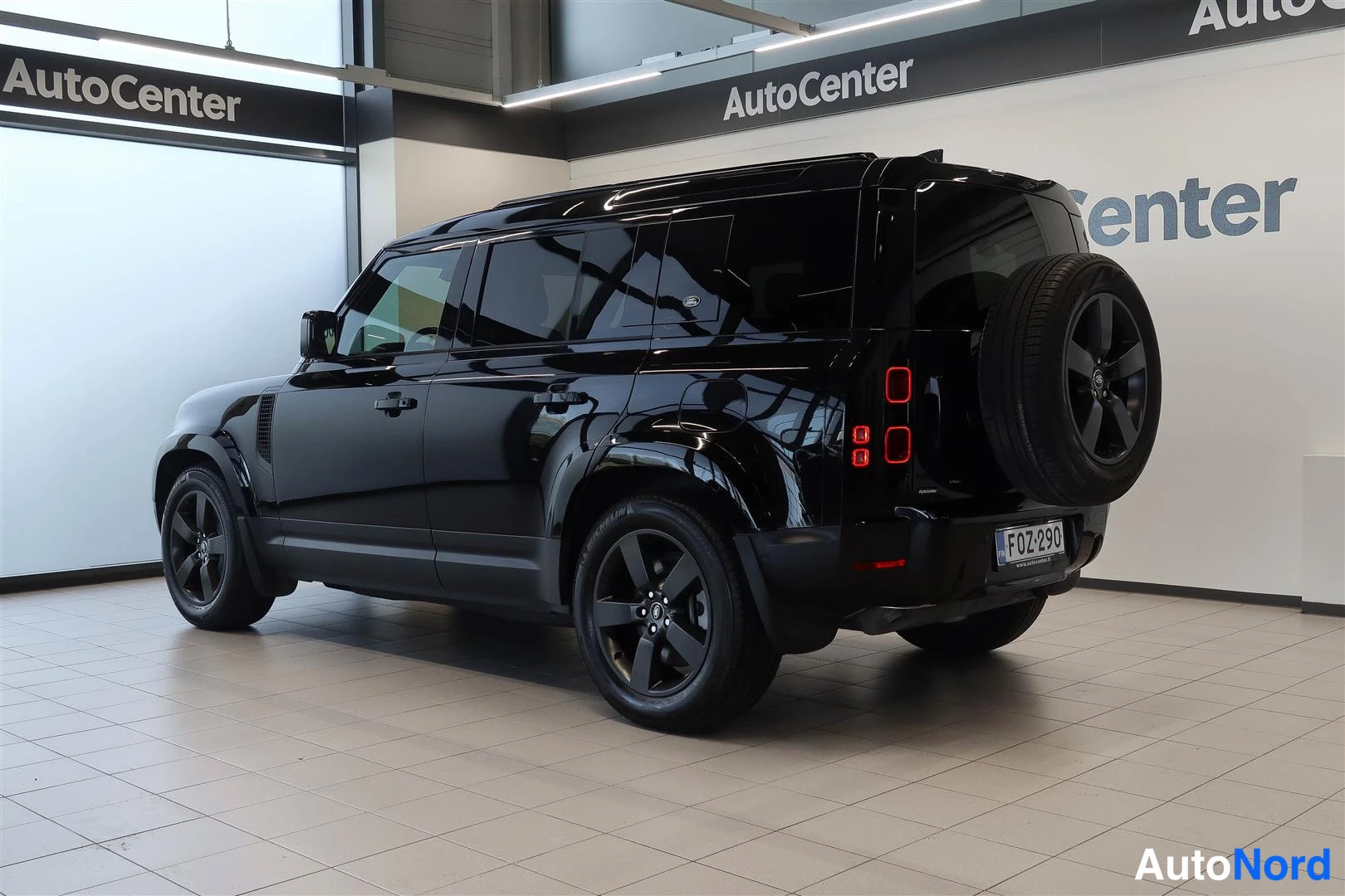 Takaviisto: Musta Land Rover Defender takaviistosta sisätiloissa; takana varapyörä, pystysuorat takavalot ja rekisterikilpi F OZ-290.