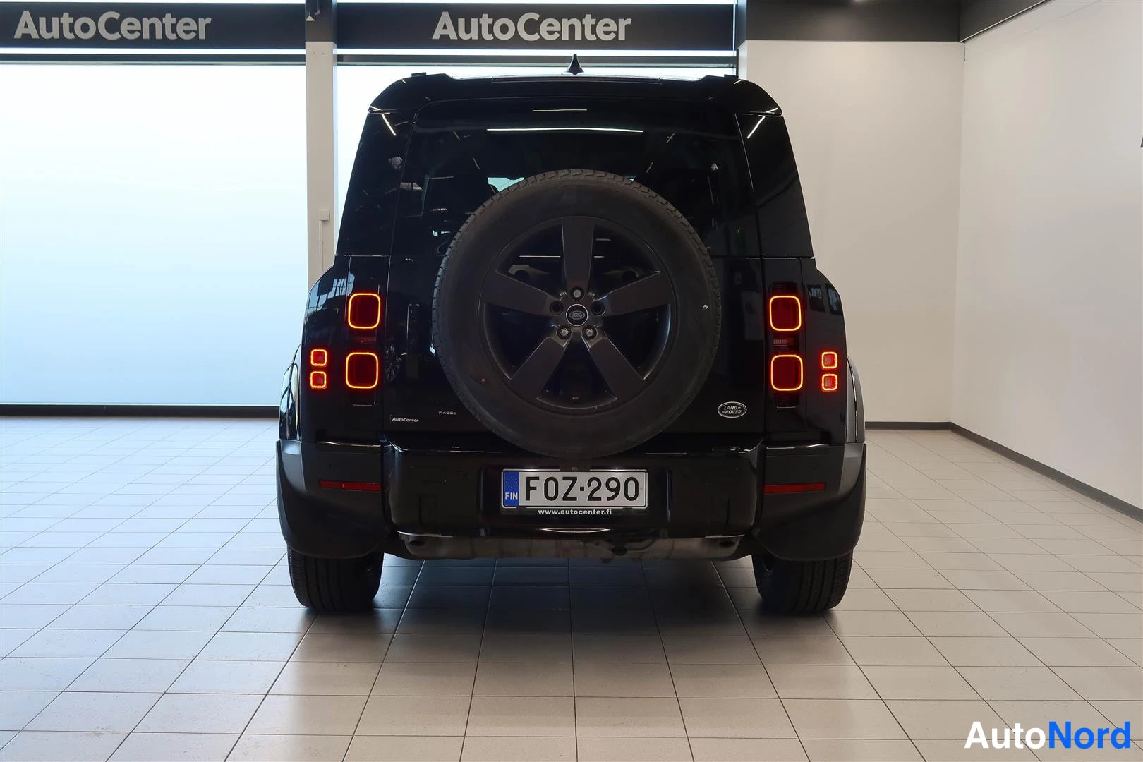 Takaa: Land Rover Defenderin takanäkymä sisätiloissa: avattu tavaratilan luukku, takaluukissa vararenkaasäiliö, musta kori, rekisterikilpi F0Z-290.