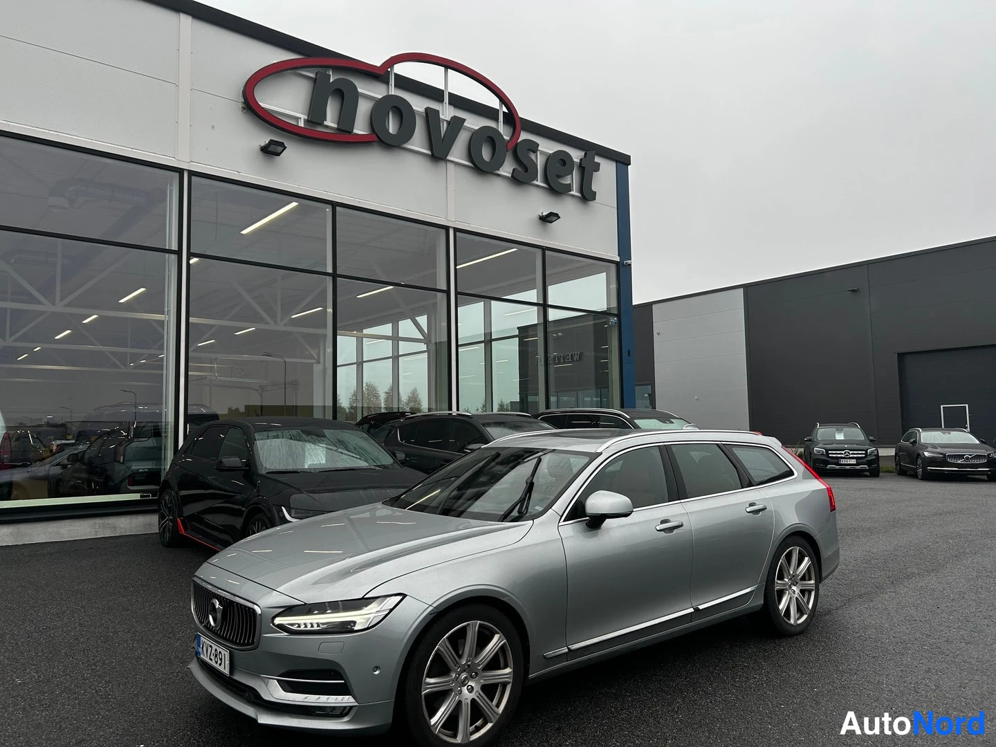 Etuviisto, nokka vasemmalle: Hopeanharmaa Volvo V90 -farmari nokka vasemmalle kääntyneenä autoliikkeen edustalla.