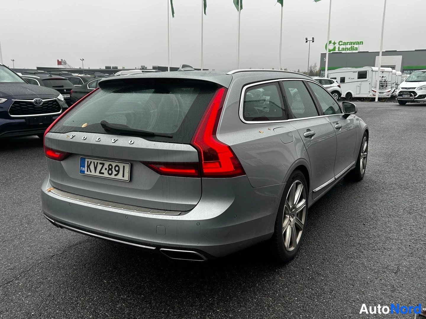 Takaviisto: Takakulma hopeanharmaasta Volvo V90 -farmarista, VOLVO-teksti ja rekisterikilpi takaovessa näkyvissä.