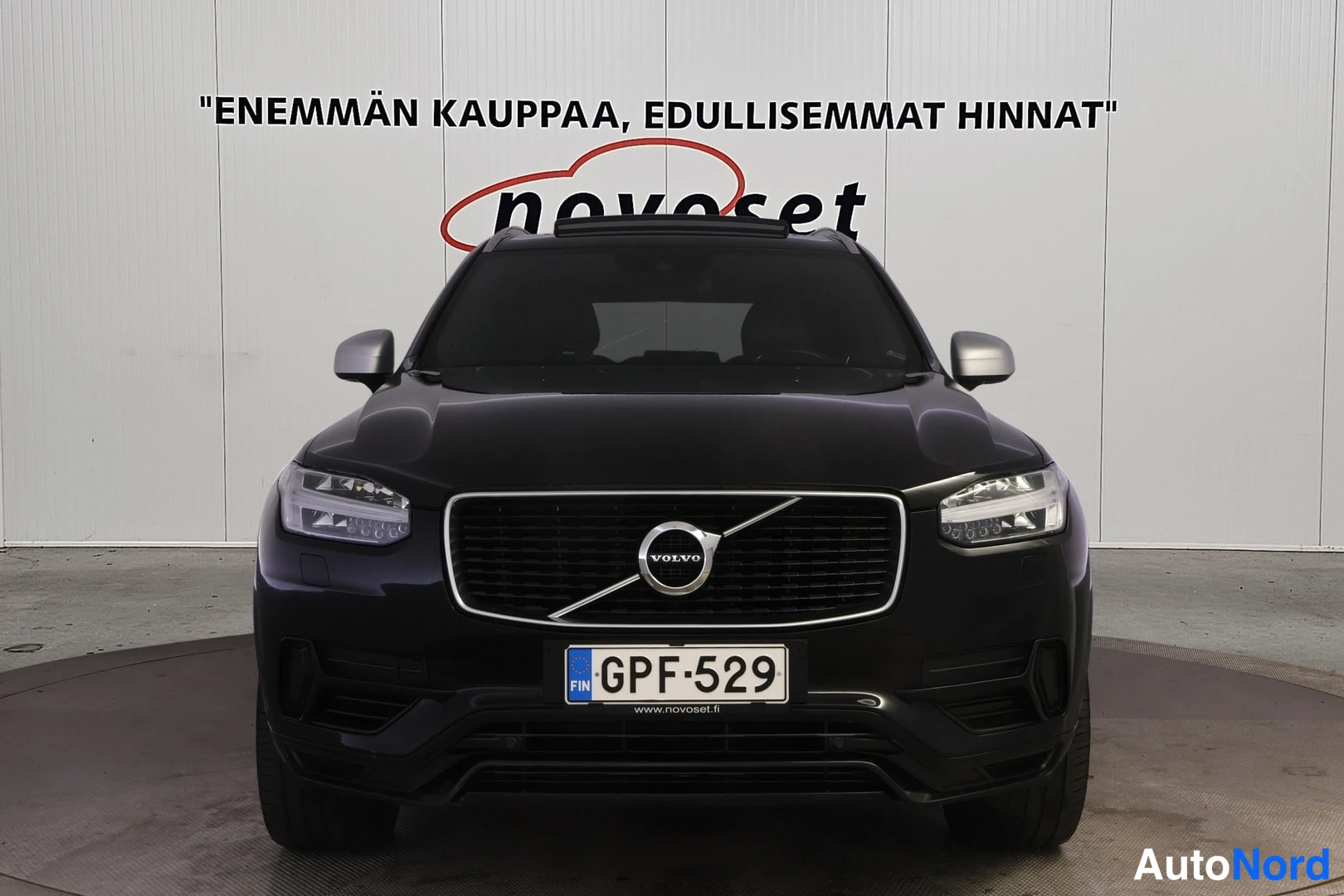 Edestä: Volvo XC90 suoraan edestä, musta koripaneli, Volvo-merkki jäähdyttäjäritilässä, rekisteritunnus.