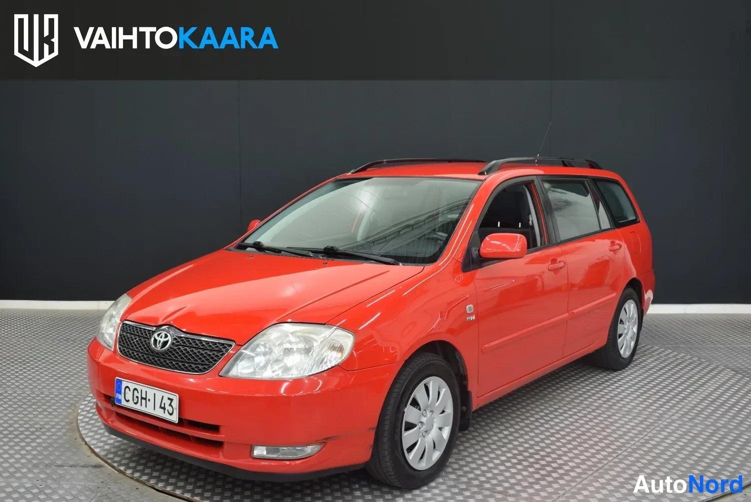 Etuviisto, nokka vasemmalle: Punaisen Toyota Corolla -farmariauton etukulmakuva studiossa, rekisterikilpi, kattotelineet näkyvissä.