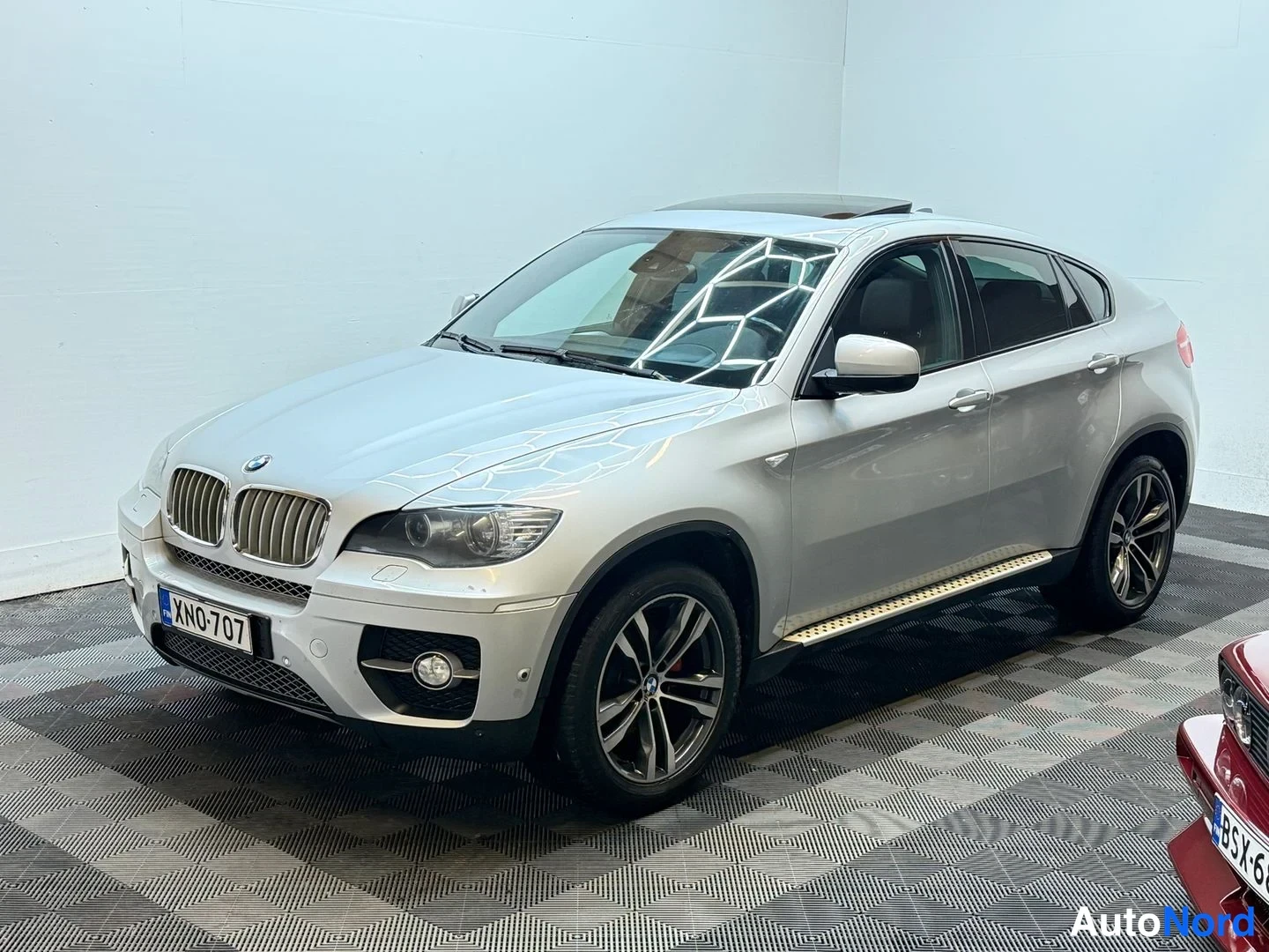 Etuviisto, nokka vasemmalle: BMW X6 kuljettajan puolelta etukulmasta kuvattuna, hopeanvärinen korimalli neontelalla ja alumiinivanteilla.