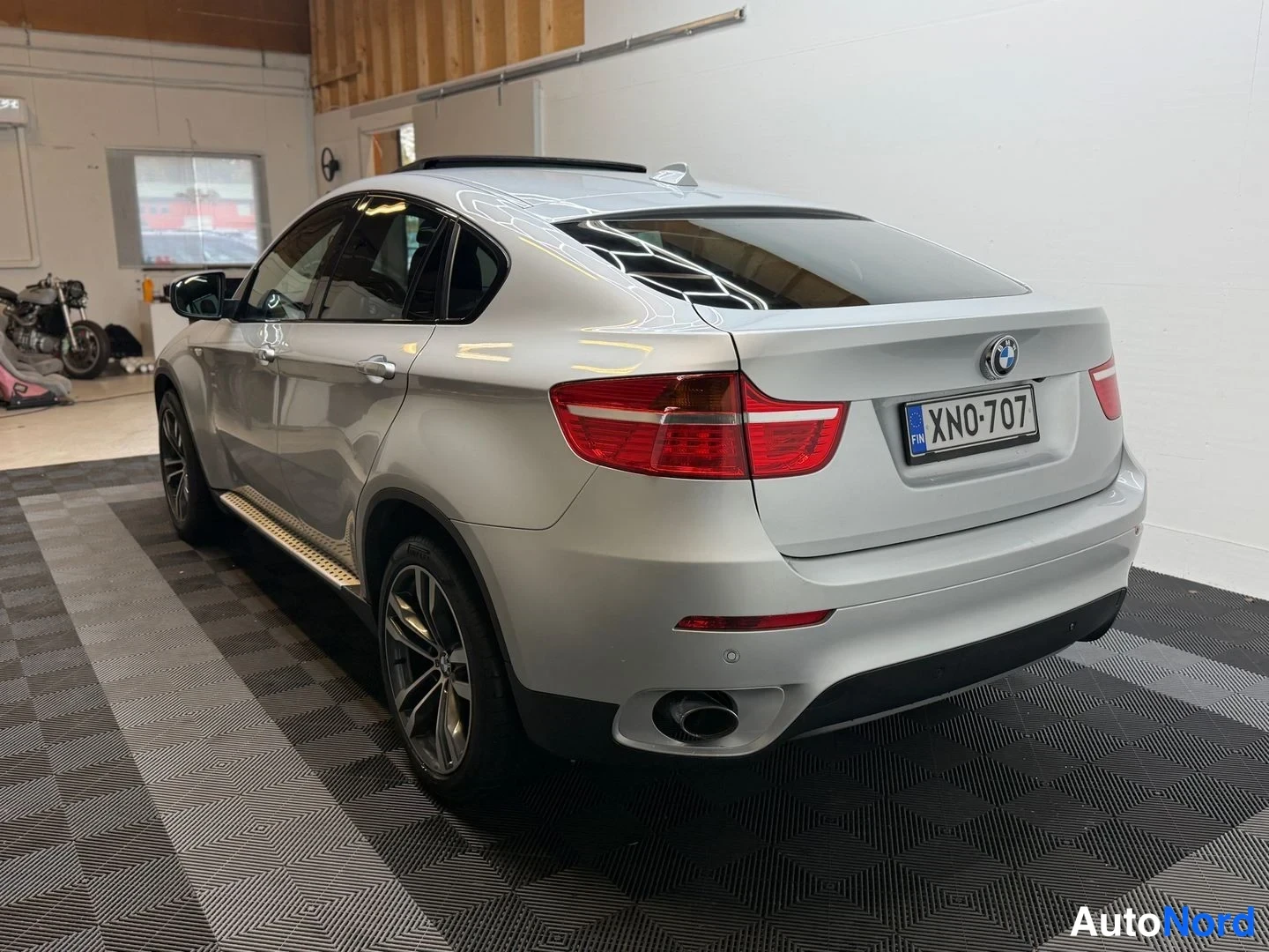Takaviisto: BMW X6:n takaosa ja vasen kylki kolmelinjaisesta kulmasta; hopeinen koripinta, punaiset takavalot, rekisterikilpi, kattoluukku ja sivulstepit näkyvät.