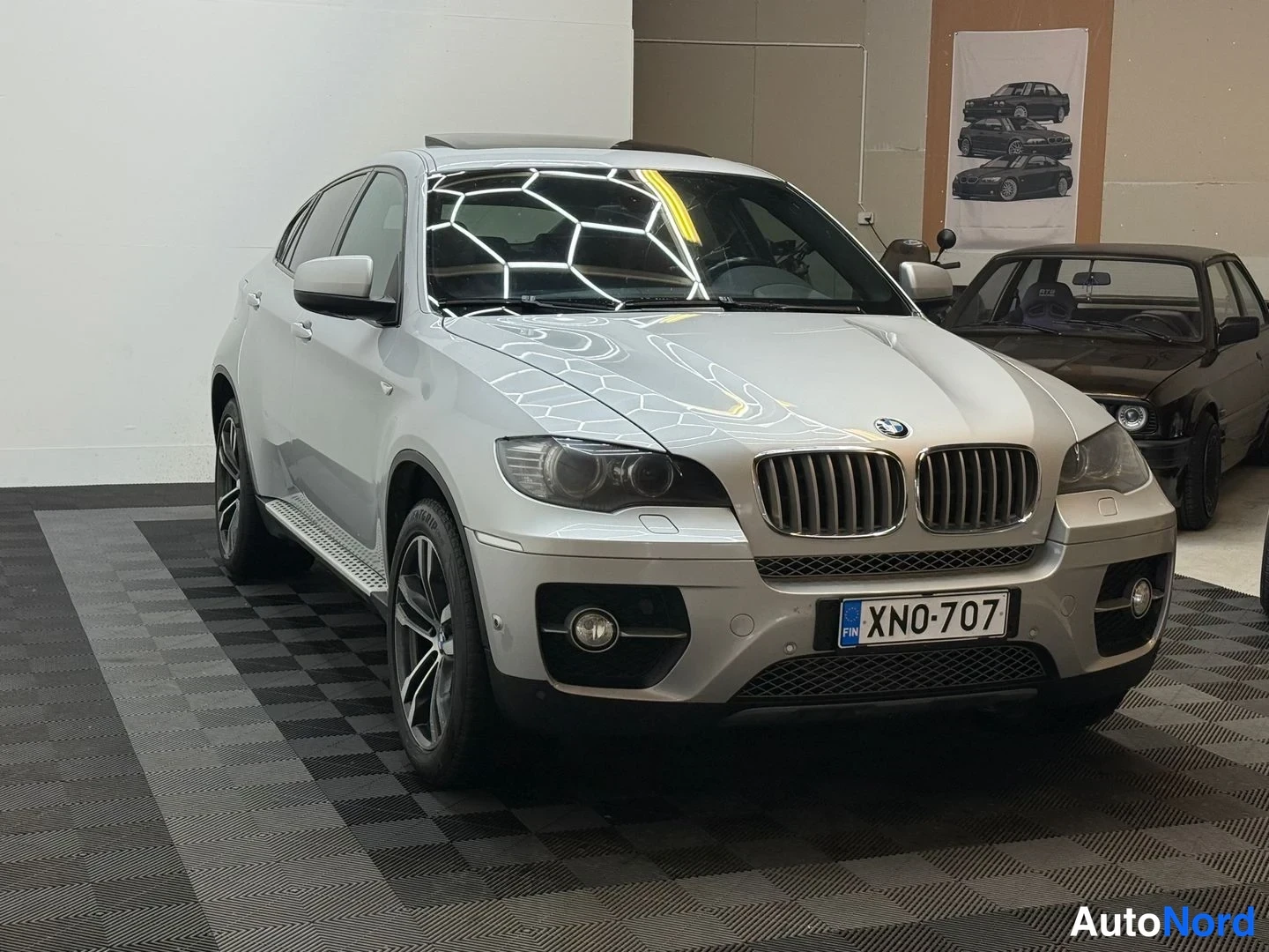 Etuviisto, nokka oikealle: BMW X6:n etuosa ja vasen kylki kolmelinjaisesta kulmasta nokka oikealla; hopeinen koripinta, munuaiskyltit, sumuvalot ja kattoluukku näkyvät.