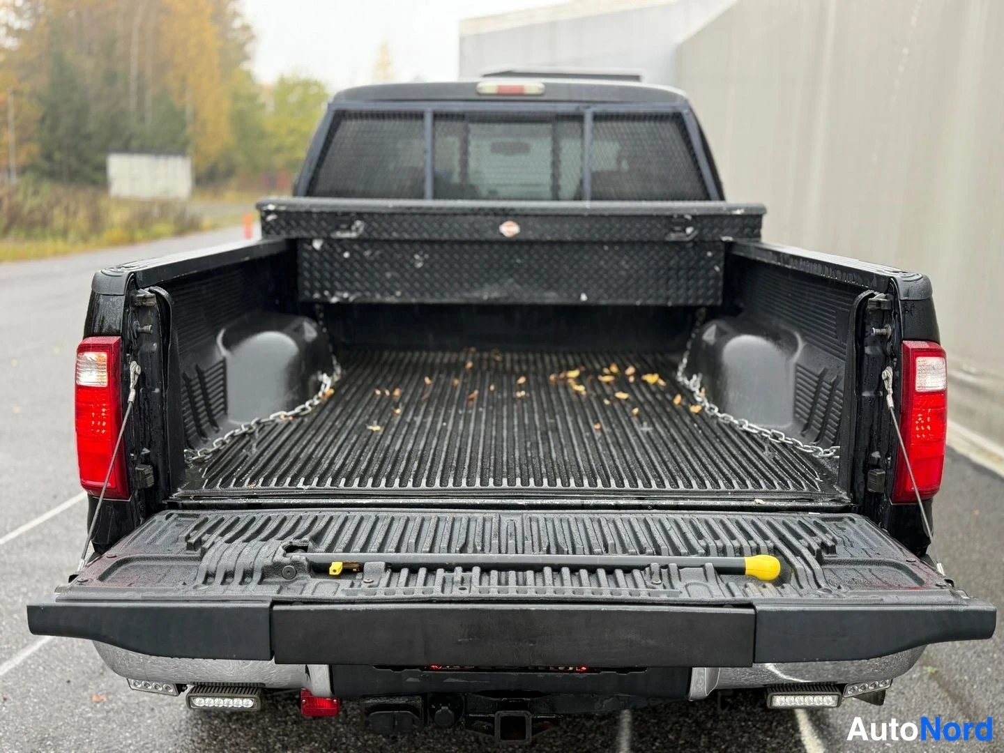 Takaa: Musta avolava-auton lava takaa kuvattuna, tailgate auki, x-ristiin kiinnitetyt varusteet lavassa.