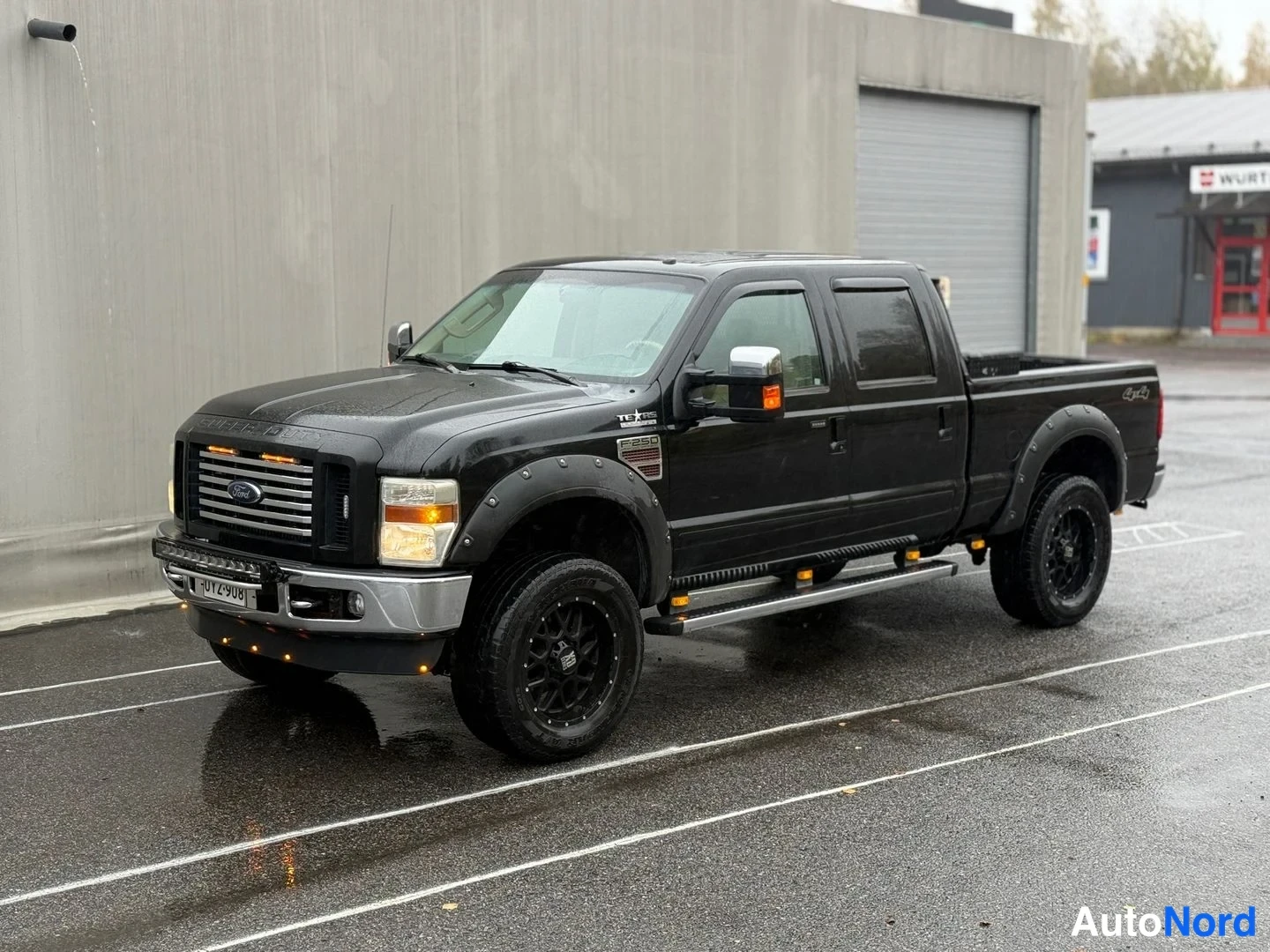 Etuviisto, nokka vasemmalle: Musta Ford Super Duty neliovinen lava-auto kulmassa nokka vasemmalle; mustat kevytmetallivanteet, lokasuojalaajenteet, sivukaiteet ja kromipeilit.