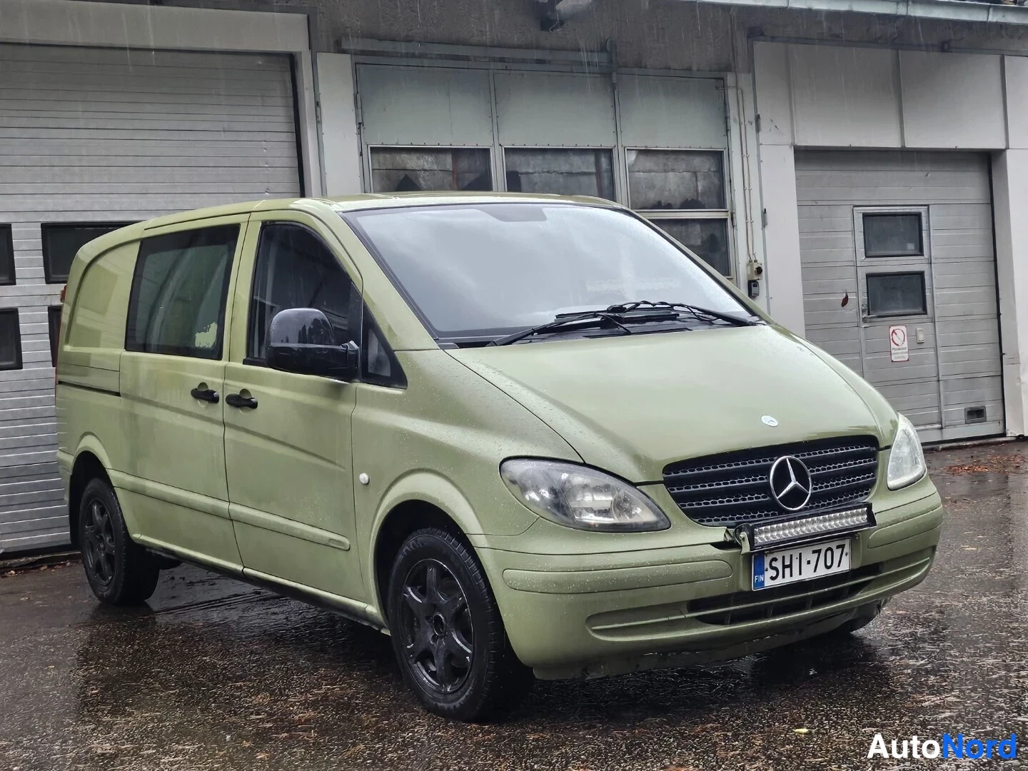 Etuviisto, nokka oikealle: Vihertävän ruskeanvärinen Mercedes-Benz Vito -pakettiauto etuviistosta rightalla; rekisterikilpi, Mercedes-tähti etusäleikössä ja lisävalo puskurissa, sa