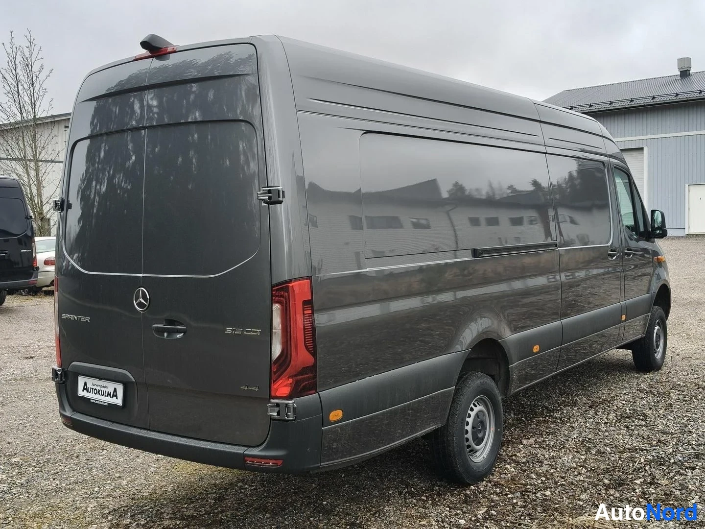 Takaviisto: Mercedes-Benz Sprinter -pakettiauto takaviistosta vasemmalta, tummanharmaa korkeakylkinen pitkä malli hiekkapohjalla.
