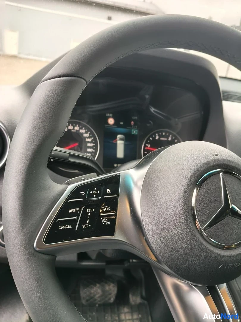 Sivulta: Ohjauspyörän lähikuva Mercedes-Benzissä: Mercedes-tähti keskellä ja vasemman pölkyn nappiryhmässä RES+, SET+, CANCEL, LIM -toiminnot, taustalla analogiset mitta