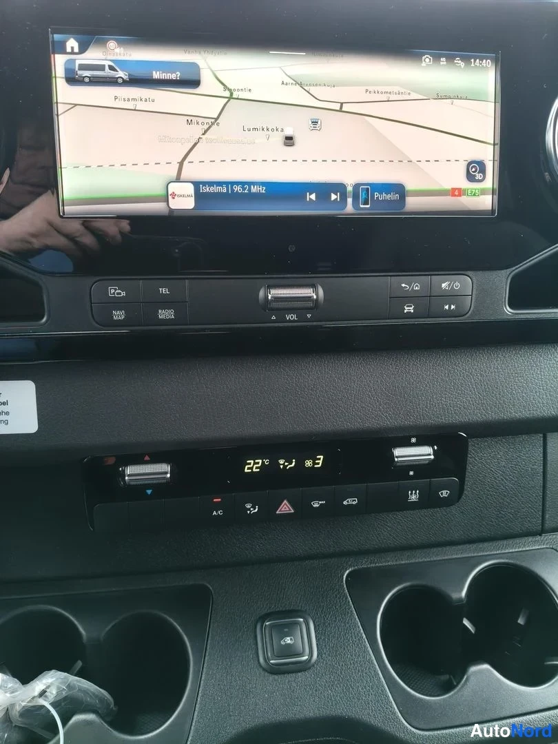 Sivulta: Mercedes-Benzin kojelaudan keskikonsoli: kartta näkyvä kosketusnäyttö, radio Iskelmä 96,2 MHz valittuna, Phone-painike, alla ilmastointipaneeli näytössä 22 °C.