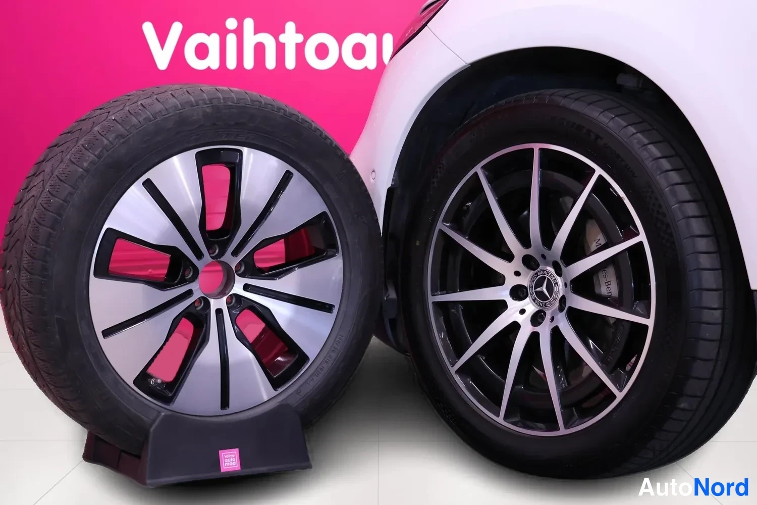Yksityiskohta: Kaksi pyörää vierekkäin: renkaan työnnetty varaosa jalustalla ja auton takapyörä monisakaraisella harkovanteella.