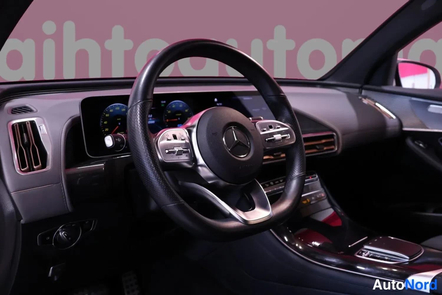 Yksityiskohta: musta Mercedes-ohjauspyörä ja paneelinäyttö, jossa analogisen tyyliset mittarit; keskikonsoli ja tuuletusaukot näkyvissä.