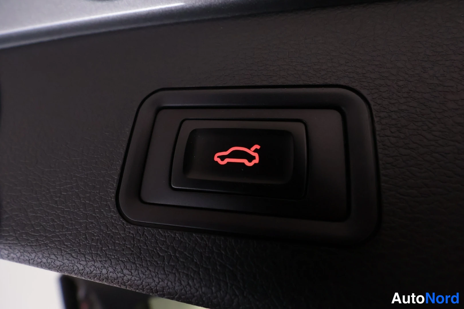 Muu: Lähikuva autoon sisäänrakennetusta painikkeesta, jonka kuvake esittää autoa takaluukku auki.