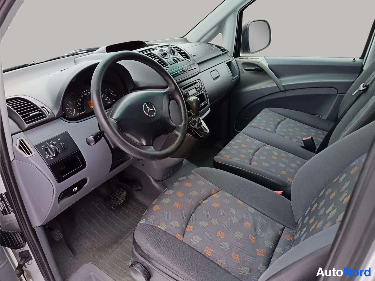 Muu: Ajetun Mercedes-Vito:n etuistuimet ja kojelauta; istuimet tummat kuviokankaalla, ohjauspyörä ja radio näkyvät.