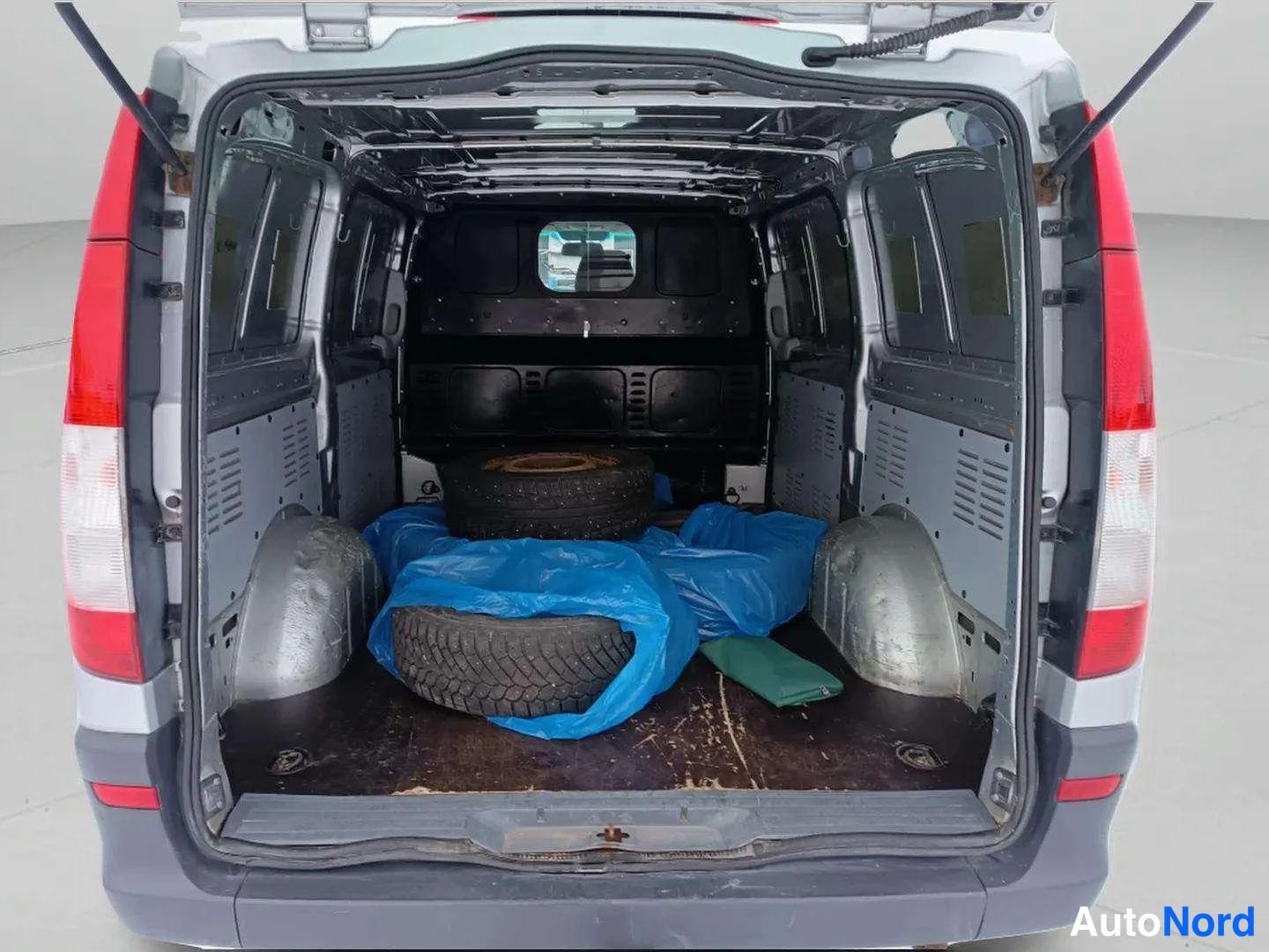 Takaa: Mercedes-Benz Vito -n Coupon takanopeus auki, lastitila ilman panelointia; lattialla kaksi rengasta ja sininen suojapeite.
