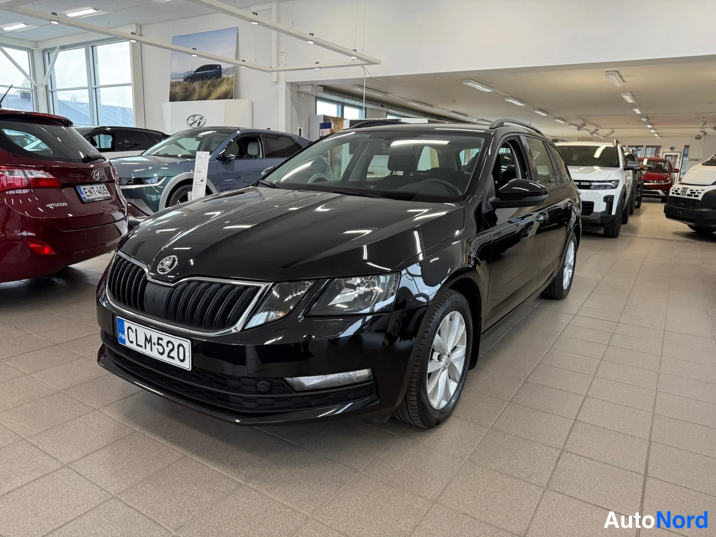 Etuviisto, nokka oikealle: Black Skoda Octavia estate shown in a showroom. Front three-quarter view from the right side showing front grille, headlights, and driver's side doors.