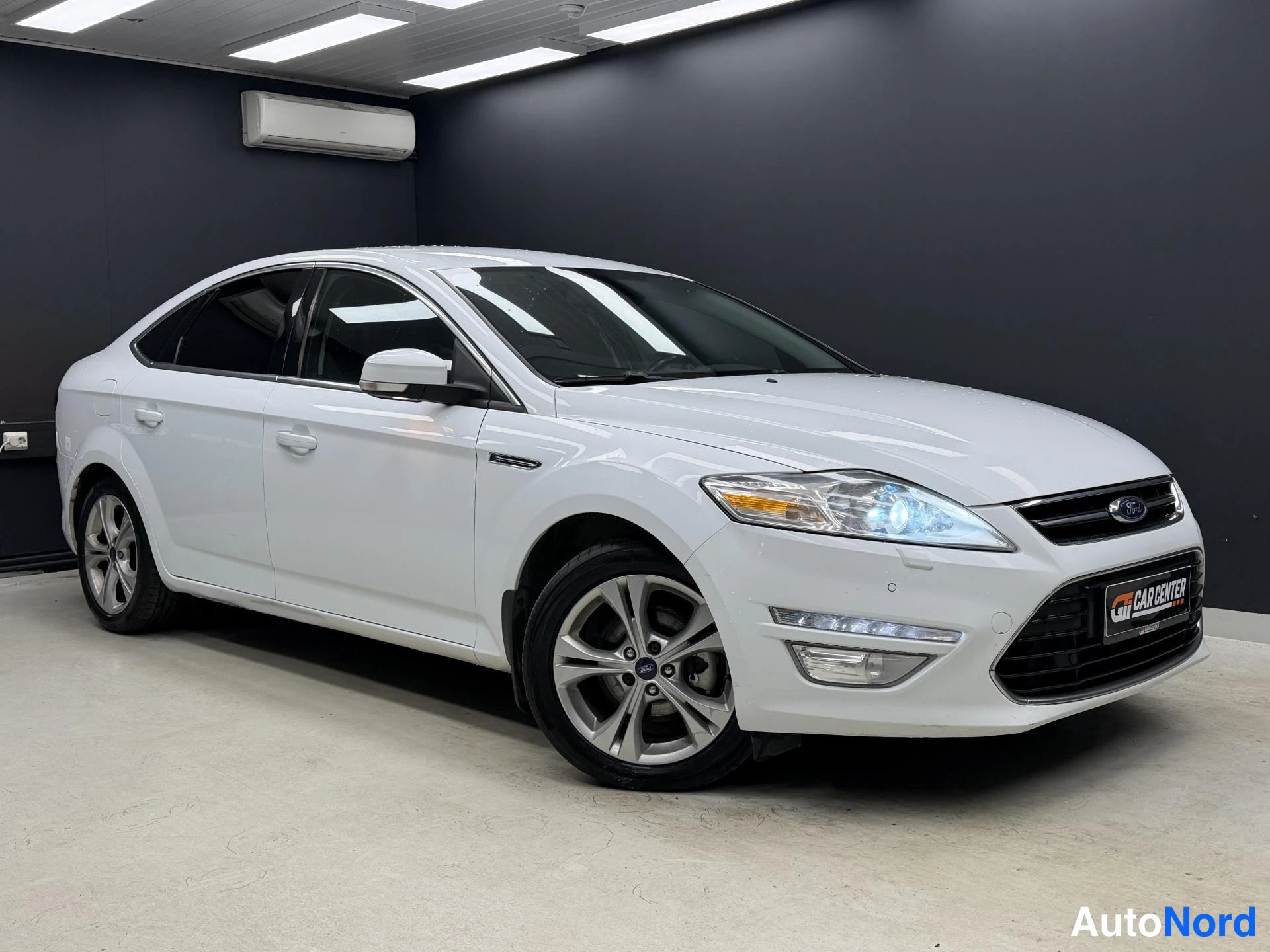 Etuviisto, nokka oikealle: Valkoinen Ford Mondeo -sedan etu‑45‑kulmakuvassa sisätiloissa, keula oikealla.