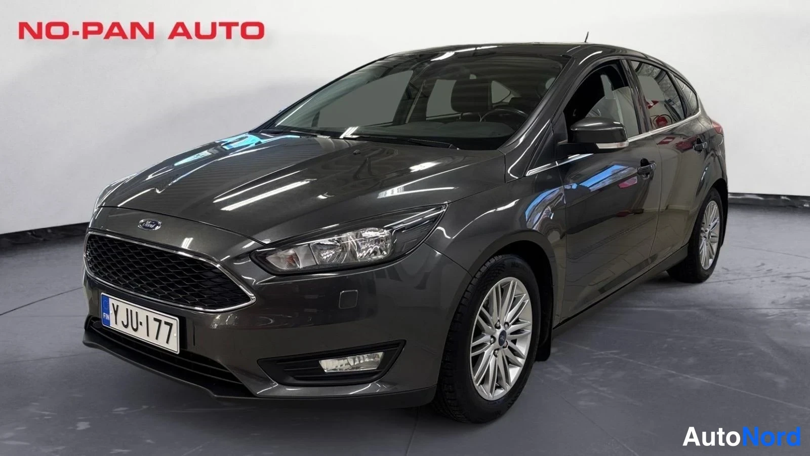 Etuviisto, nokka vasemmalle: Auton etuosa ja vasen sivu kuvattuna kolmesta neljäsosakulmasta, harmaa Ford-hatchback, rekisteritunnus.