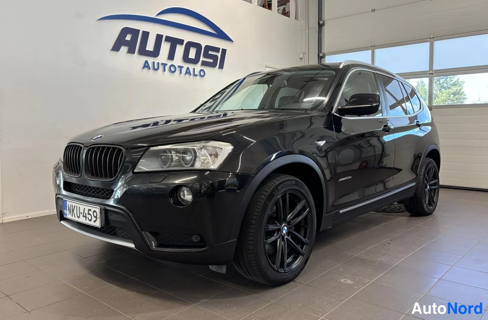 Etuviisto, nokka vasemmalle: BMW X3, musta, auton etukulma vasemmalta, rekisteritunnus, Autosi Autotalon sisätiloissa.