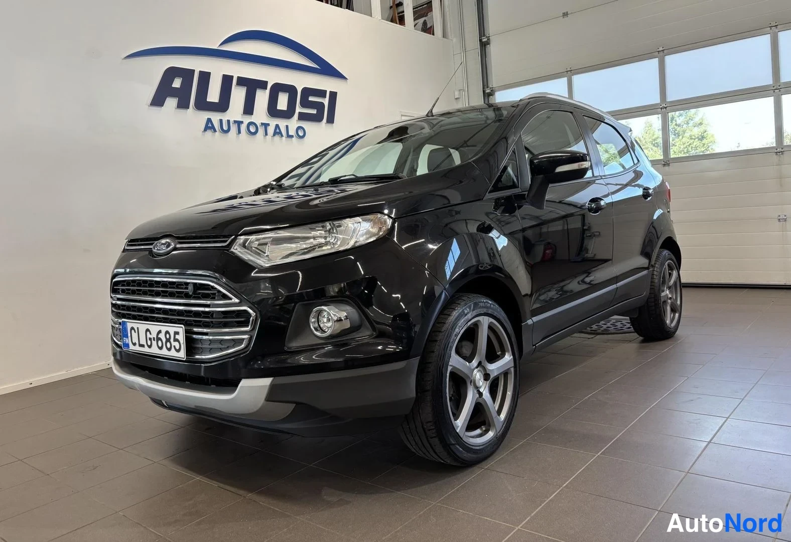 Etuviisto, nokka vasemmalle: Musta Ford EcoSport -henkilöauto etuviistosta autotallin sisällä, Autosi Autotalo -kyltti taustalla.