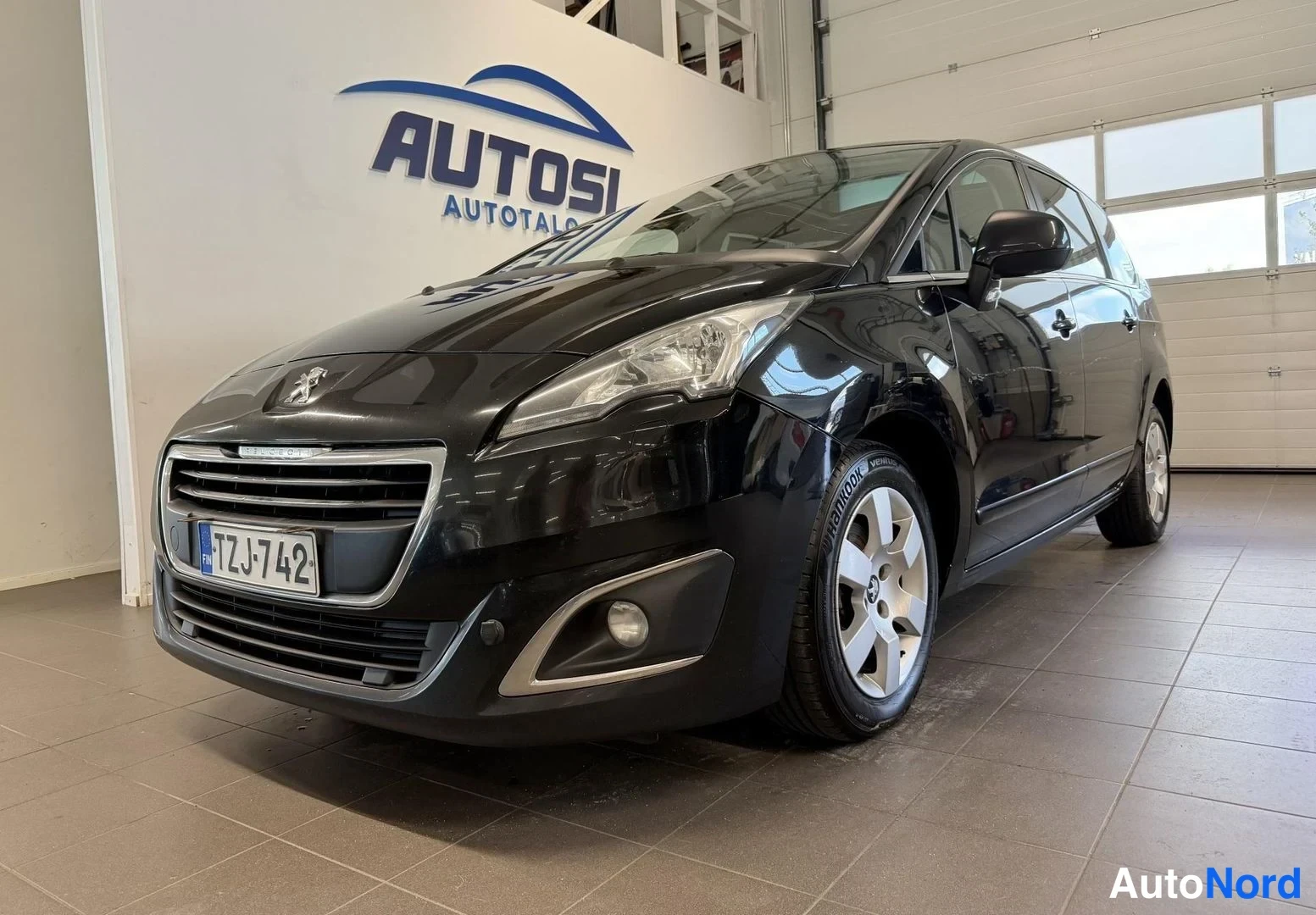 Etuviisto, nokka vasemmalle: Mustan Peugeot 5008:n etukulma autonhallissa, rekisterikilpi.