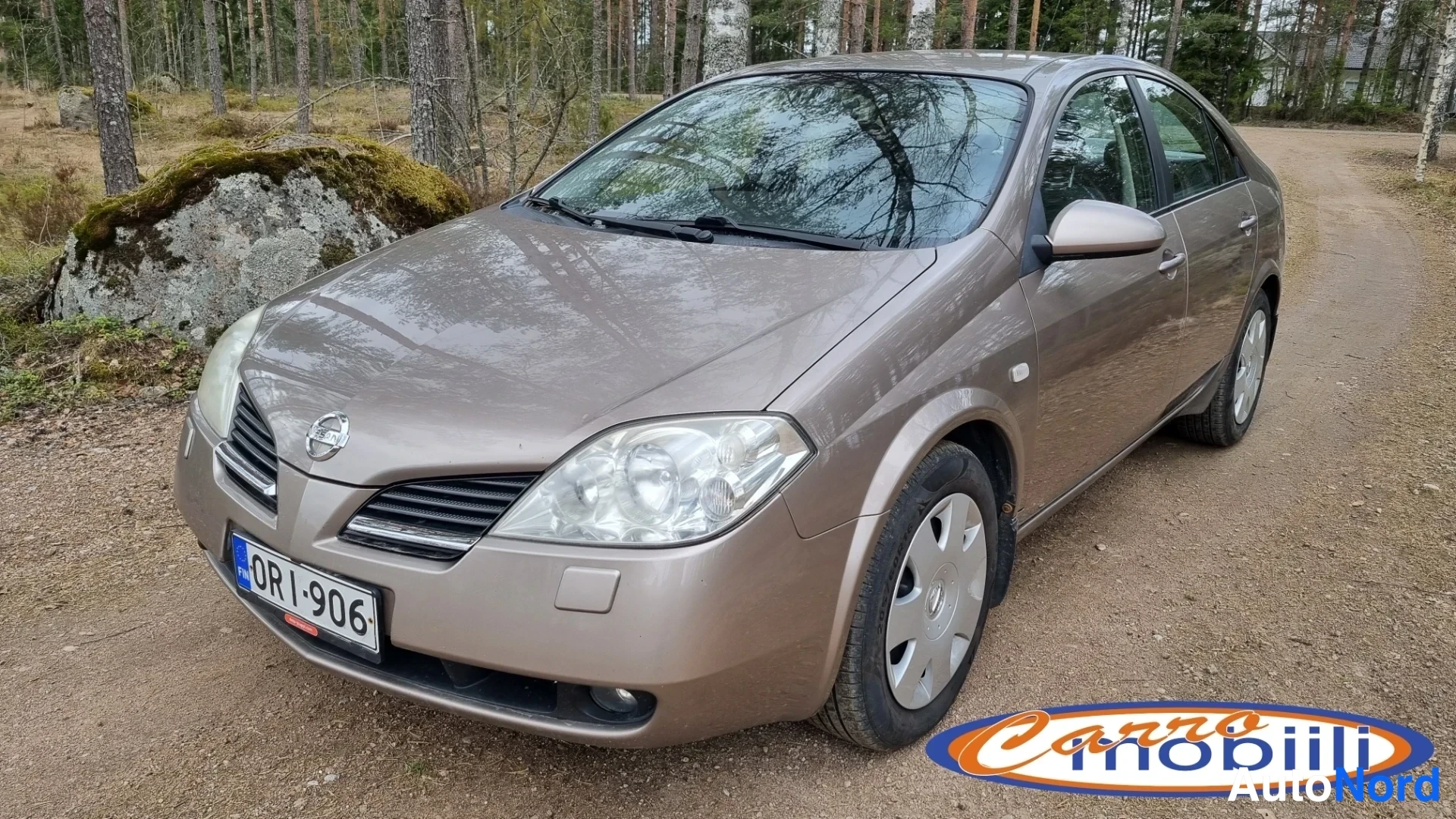 Etuviisto, nokka vasemmalle: Beige Nissan Primera -sedanin etukulmanäkymä soratiellä, rekisteritunnus.